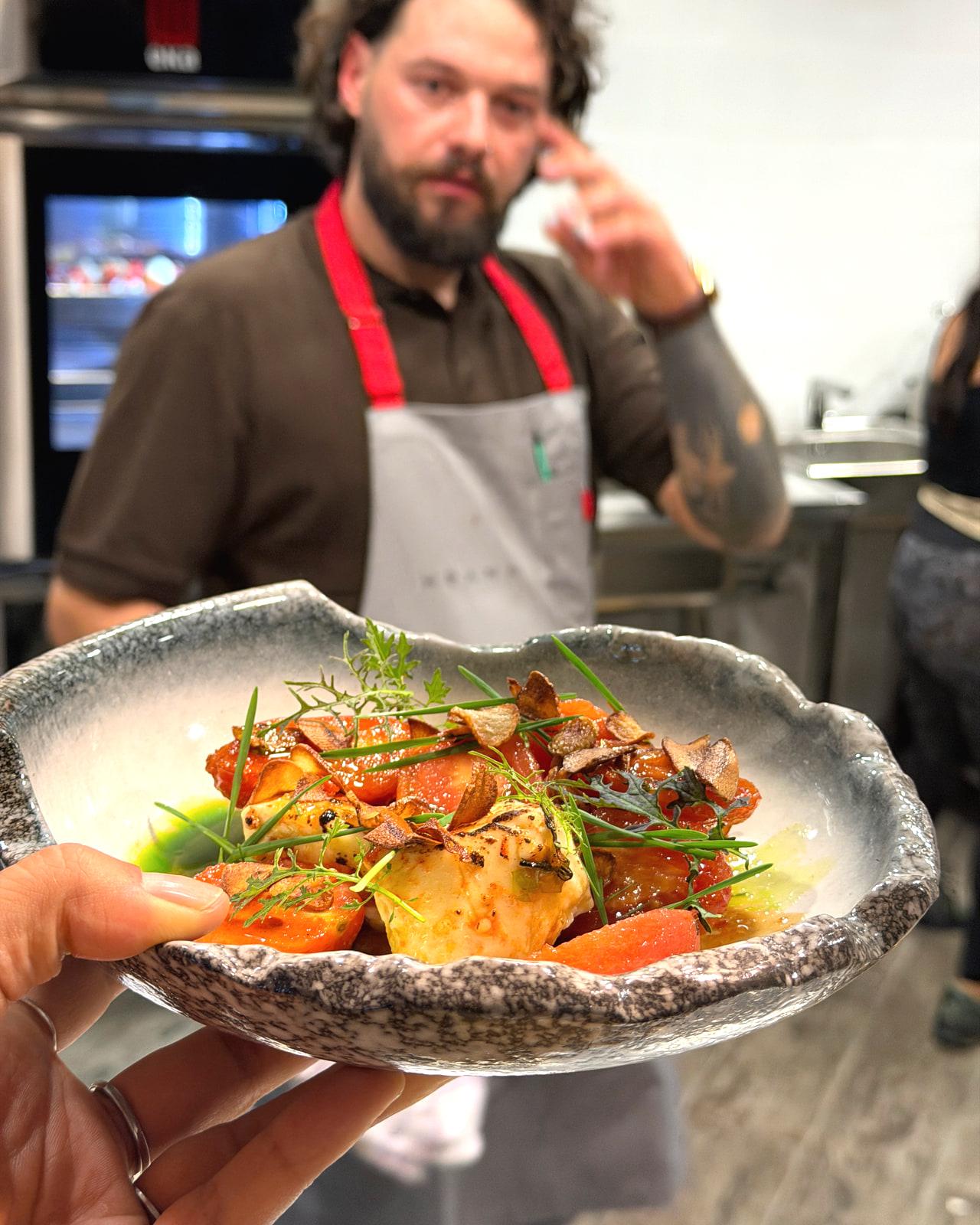 Ciotola di pomodori arrosto, formaggio e chips di aglio tenuta in mano da uno chef di HRANA
