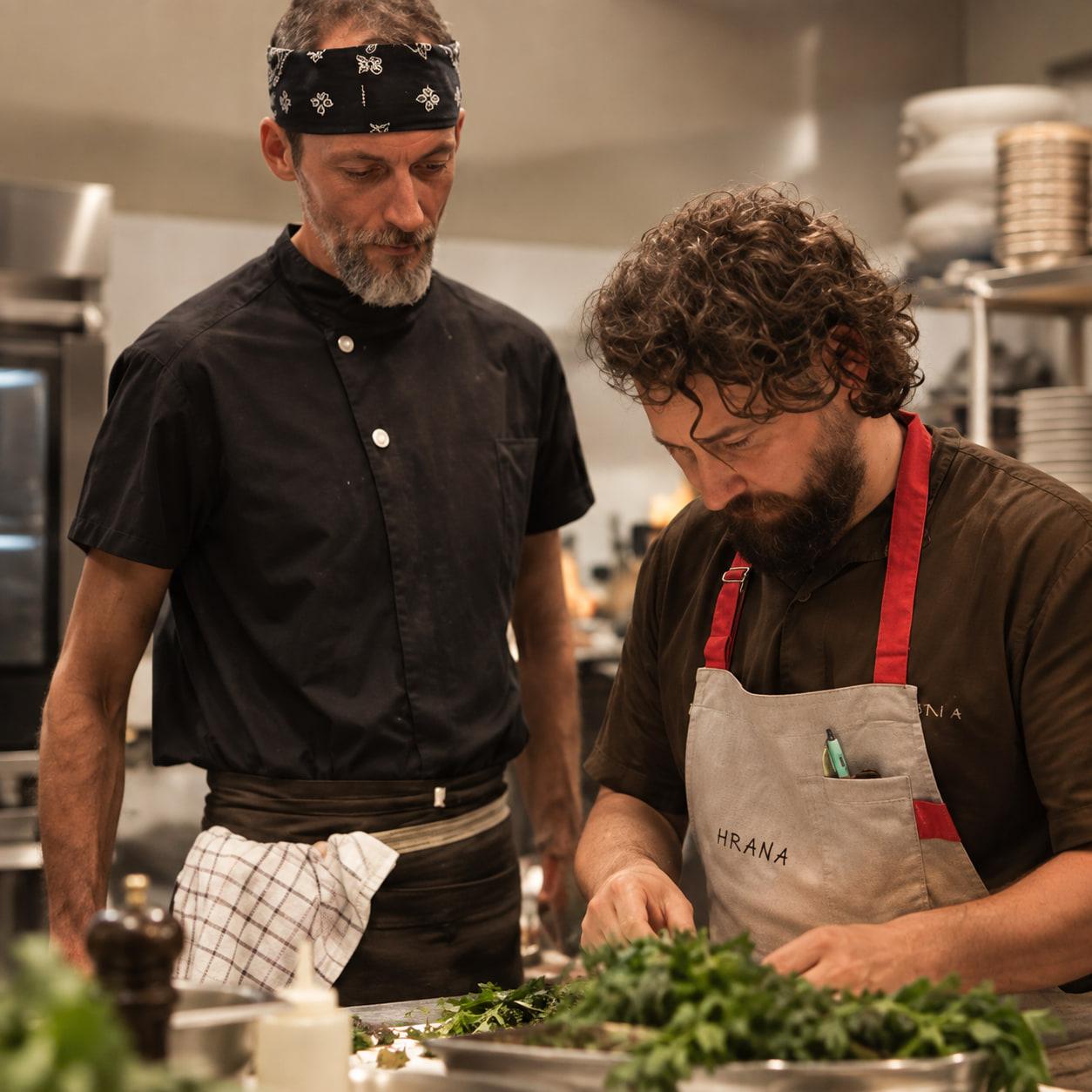 Lo chef Adrian Bașa rifinisce un piatto con germogli freschi nella cucina di HRANA, accanto a un collega della squadra