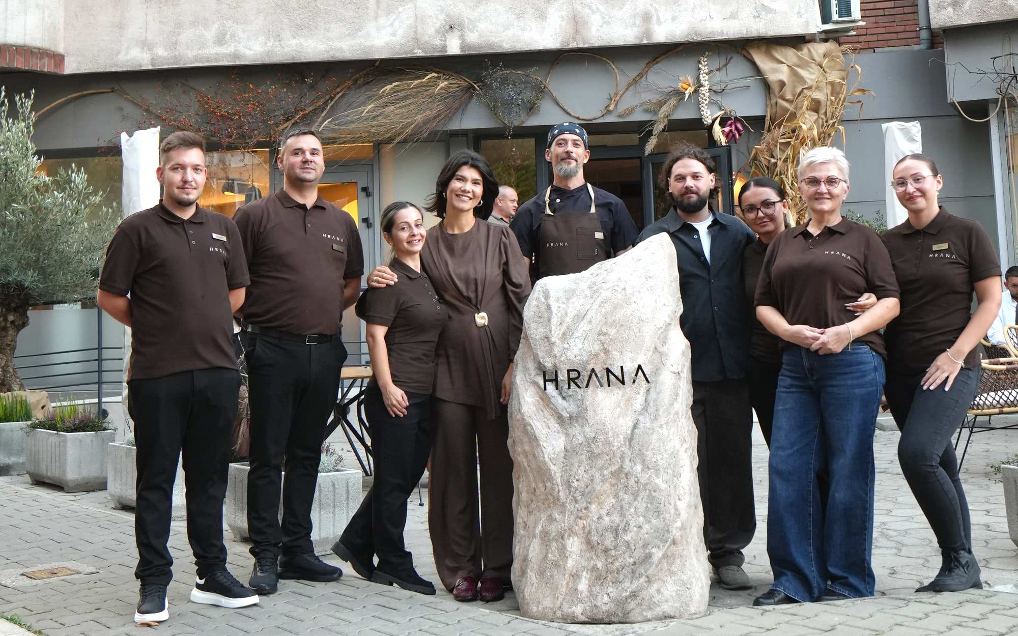 La squadra di HRANA davanti alla pietra con il logo, all'ingresso del ristorante a Hunedoara