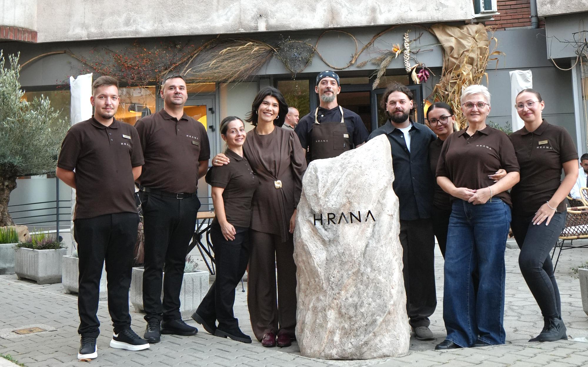 La squadra di HRANA davanti alla pietra con il logo, all'ingresso del ristorante a Hunedoara