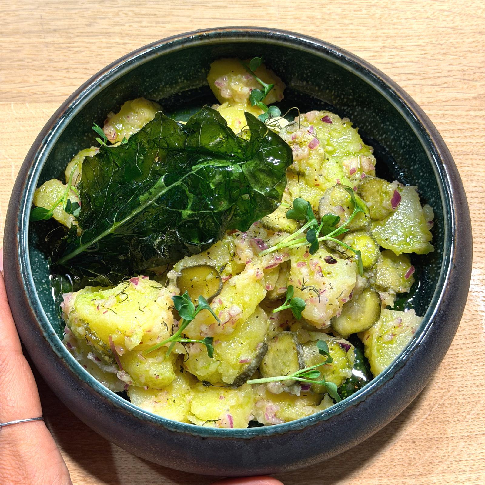 Insalata di patate con cetriolini, cipolla rossa e germogli in una ciotola di ceramica verde