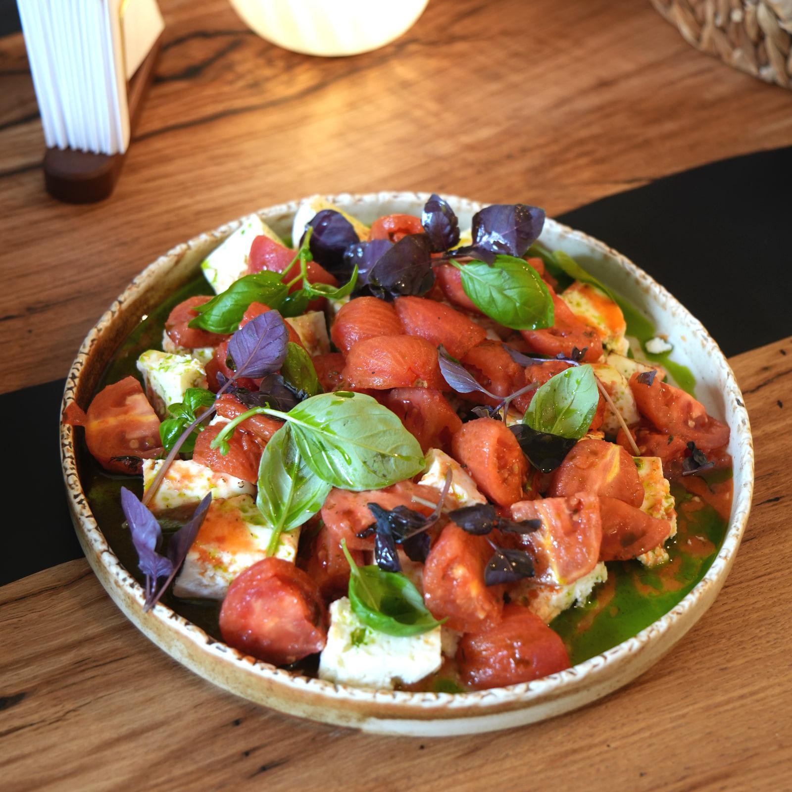 Insalata di pomodori con formaggio e basilico su un piatto di ceramica, da HRANA