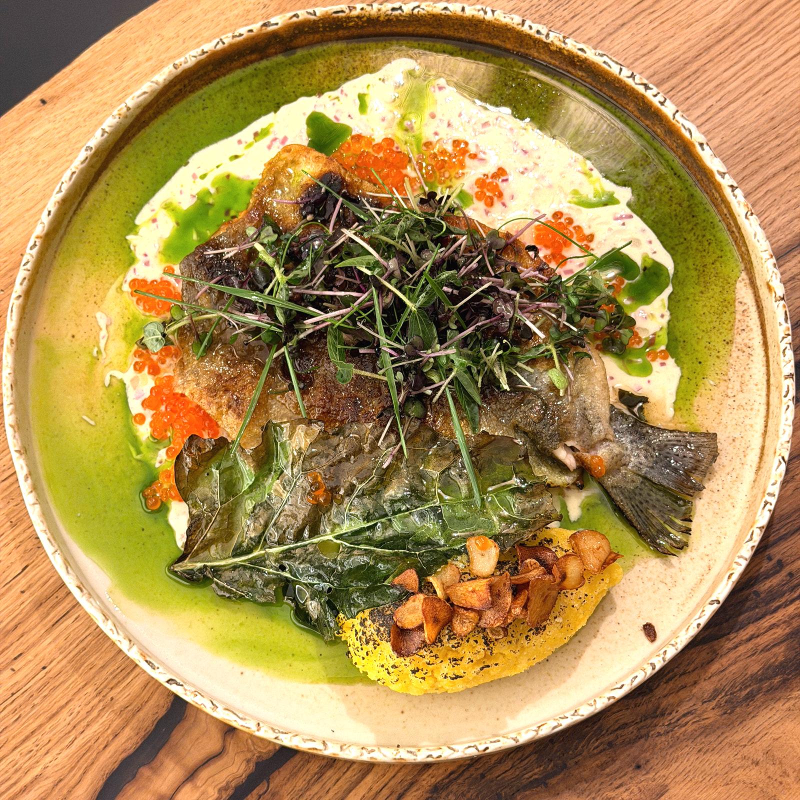 Trota con polenta, aglio fritto, uova di pesce e micro-germogli su un piatto di ceramica